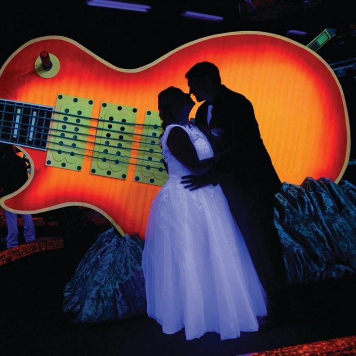 Bride and groom holding each other in front of orange guitar at Rock N Roll Wedding Chapel in Las Vegas. 
